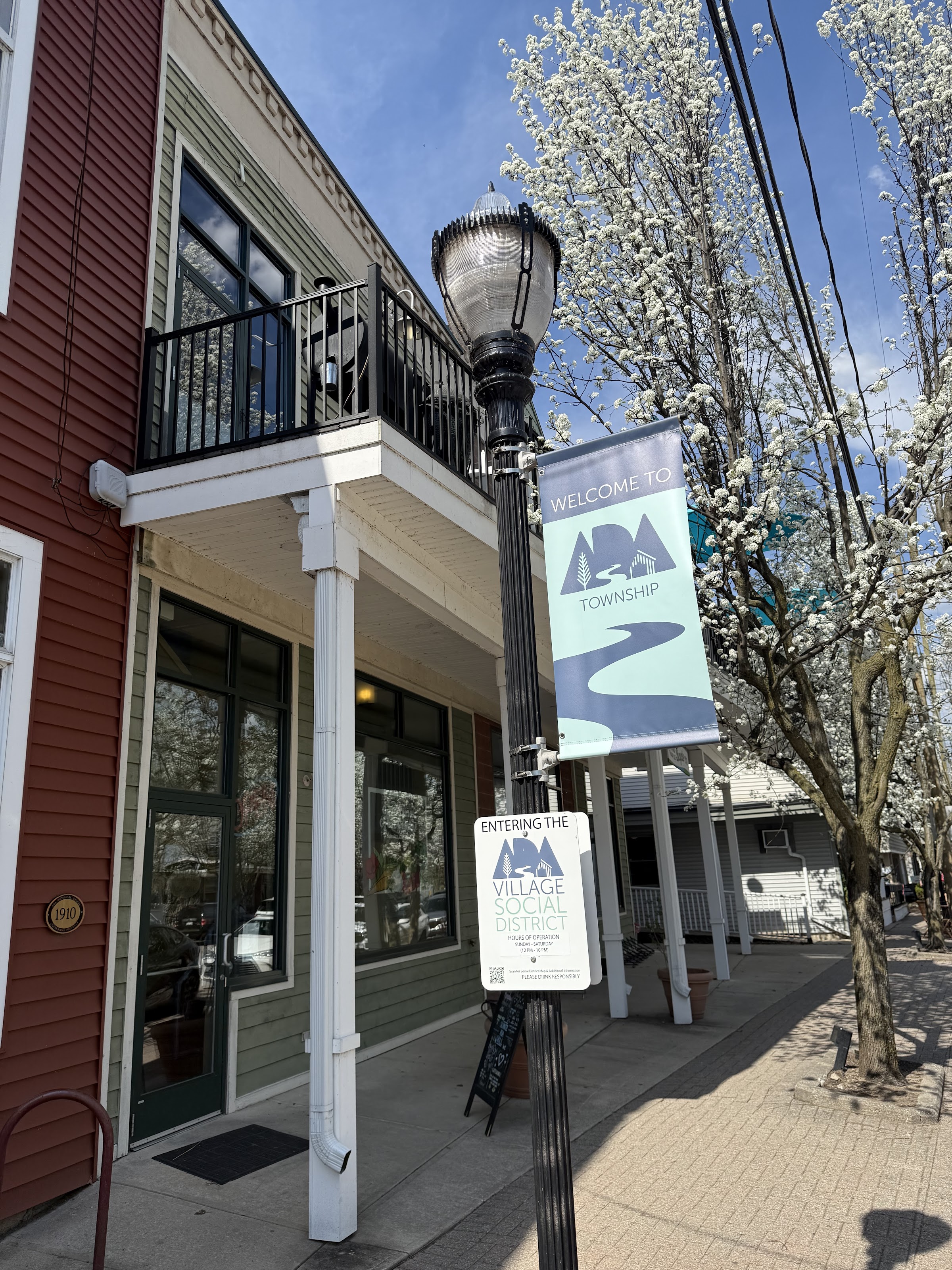 The Schnitz storefront in Ada Village — red brick, spring blossoms, and the Ada Township welcome banner